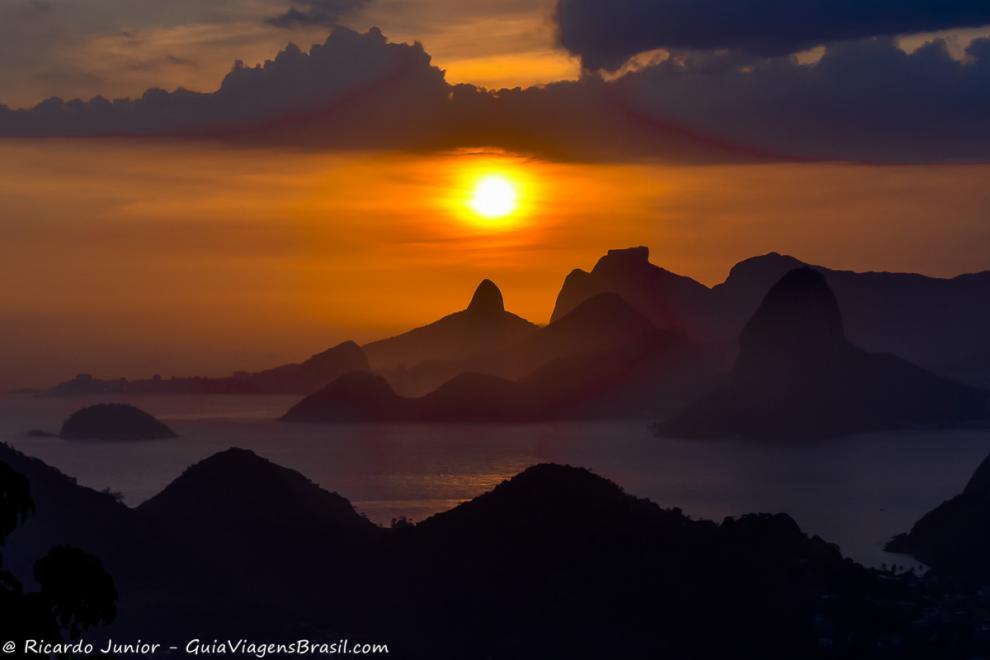 Imagem do por do sol com céu alaranjado vista dos morros do Rio.